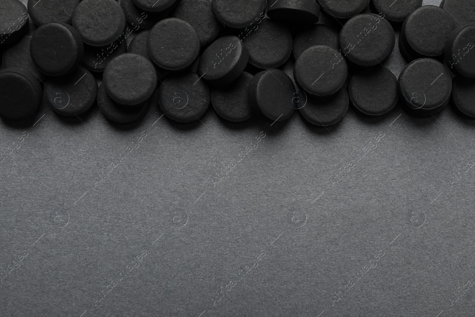 Photo of Activated charcoal pills on grey background, flat lay with space for text. Potent sorbent