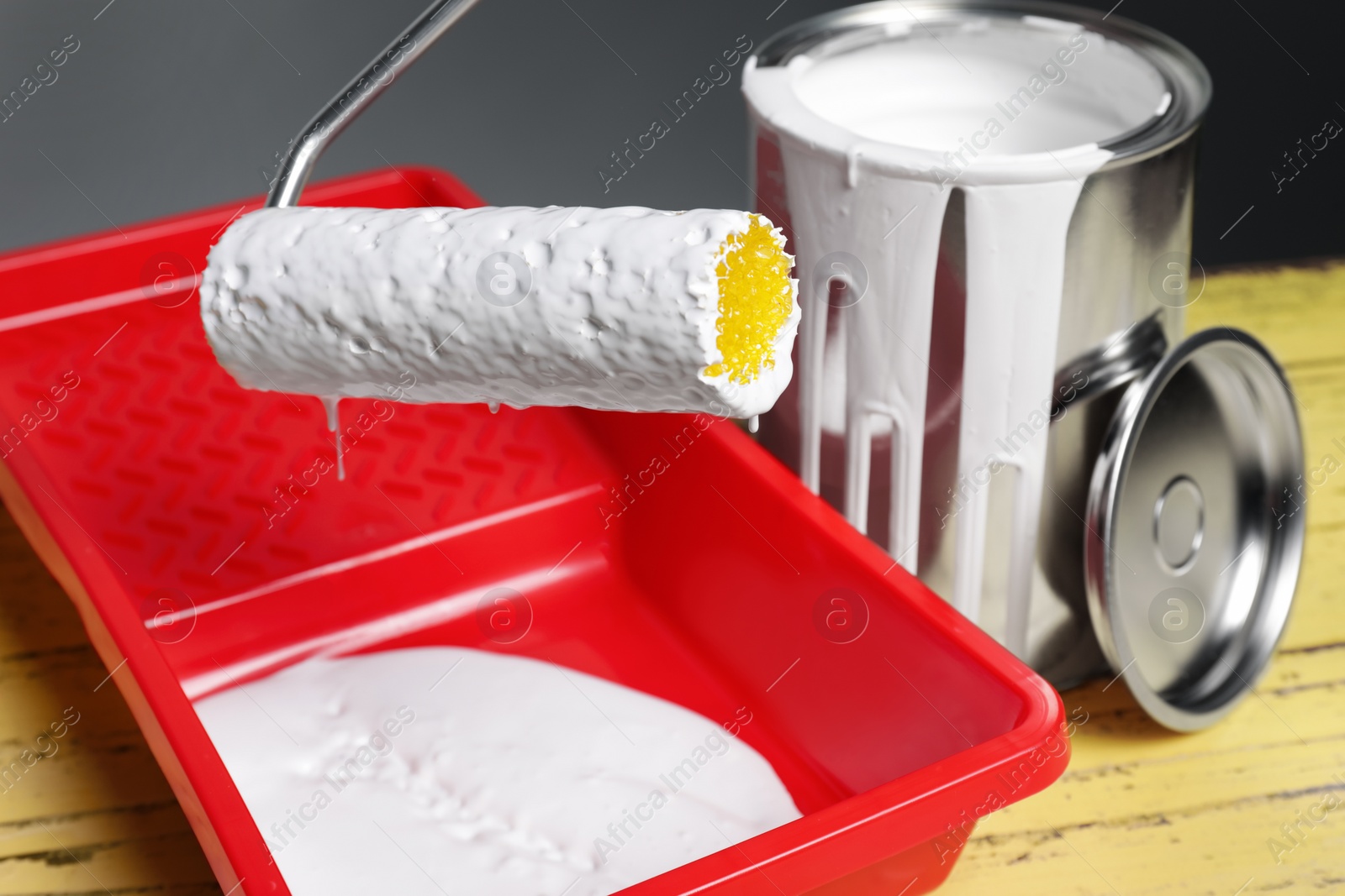 Photo of Can of paint, roller and tray on yellow wooden table, closeup