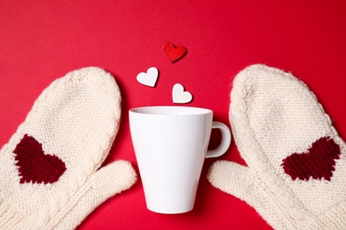 Photo of Knitted mittens, cup and paper hearts on red background, flat lay