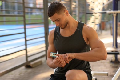 Attractive serious man checking pulse after training on sports ground