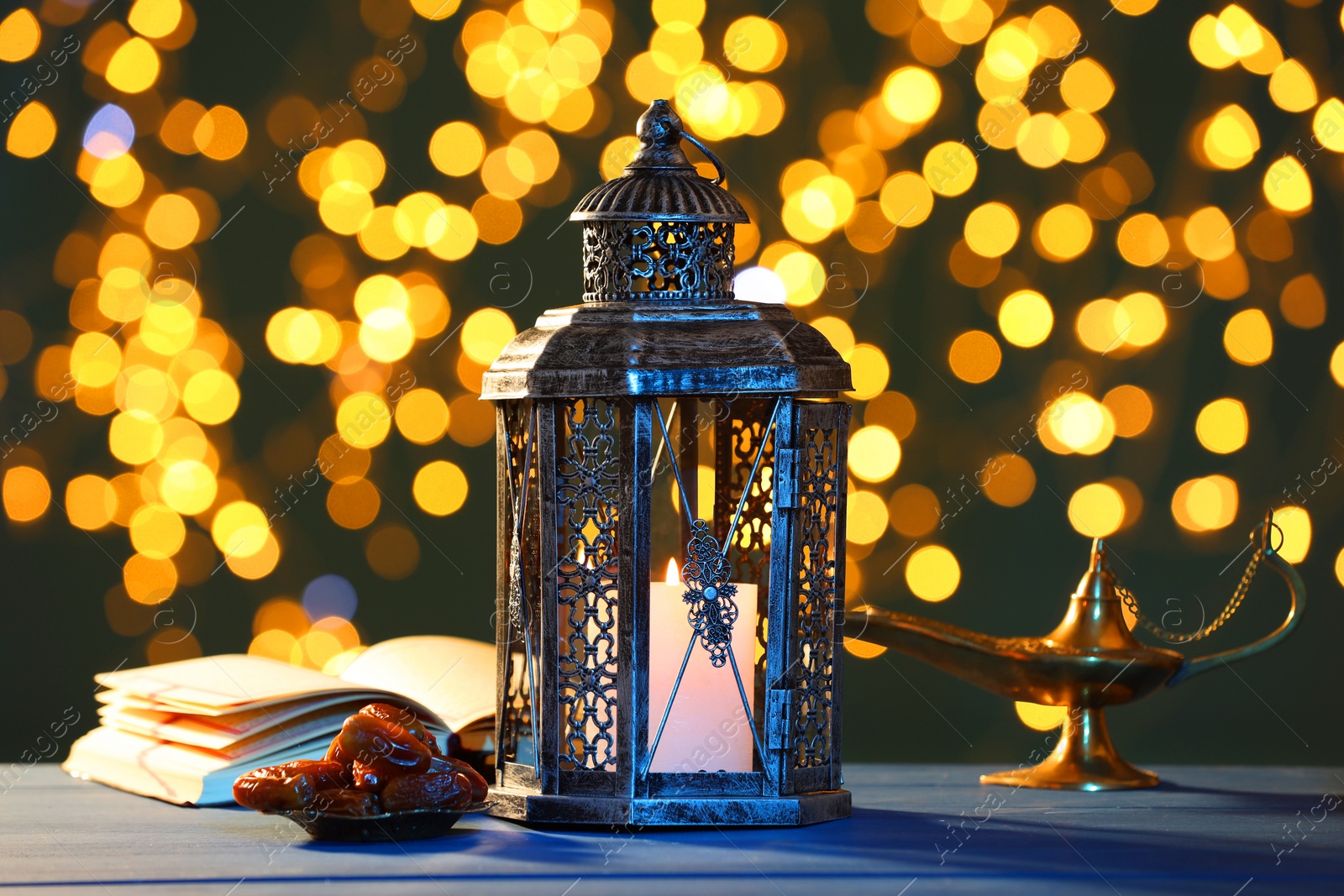 Photo of Arabic lantern, Quran, dates and Aladdin magic lamp on table against blurred lights at night