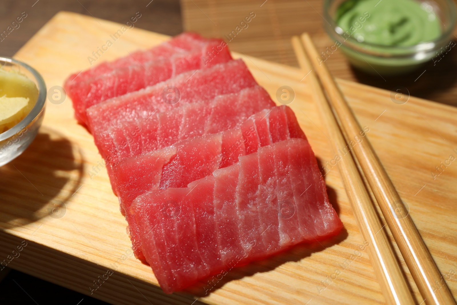 Photo of Tasty sashimi (pieces of fresh raw tuna) and chopsticks on wooden board, closeup