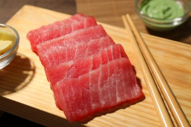 Photo of Tasty sashimi (pieces of fresh raw tuna) and chopsticks on wooden board, closeup