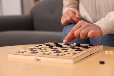 Photo of Woman playing checkers at wooden table indoors, closeup
