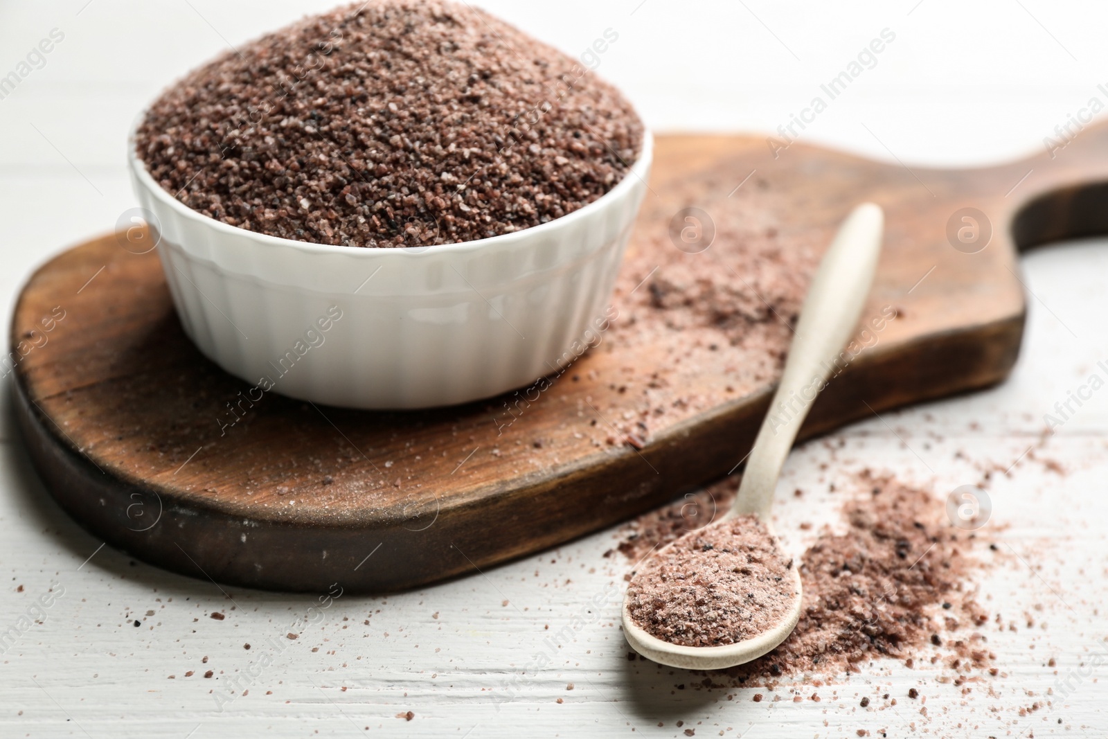 Photo of Spoon and bowl with black salt on white wooden table