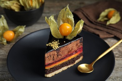 Photo of Piece of tasty cake decorated with physalis fruit on wooden table, closeup