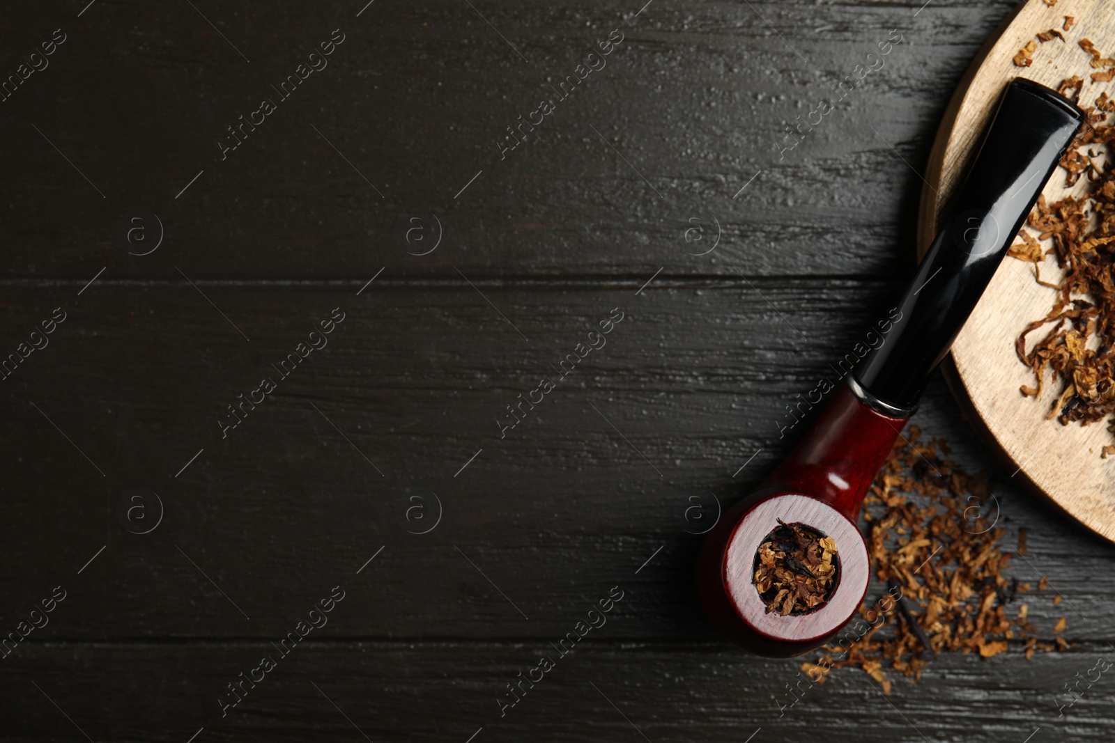 Photo of Smoking pipe and dry tobacco on dark wooden table, flat lay. Space for text