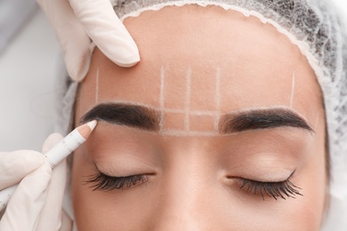 Photo of Young woman getting prepared for procedure of permanent eyebrow makeup in tattoo salon, closeup