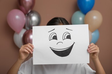 Photo of Little girl hiding behind sheet of paper with laughing face in decorated room