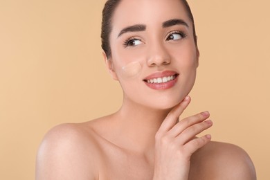 Woman with swatch of foundation on face against beige background