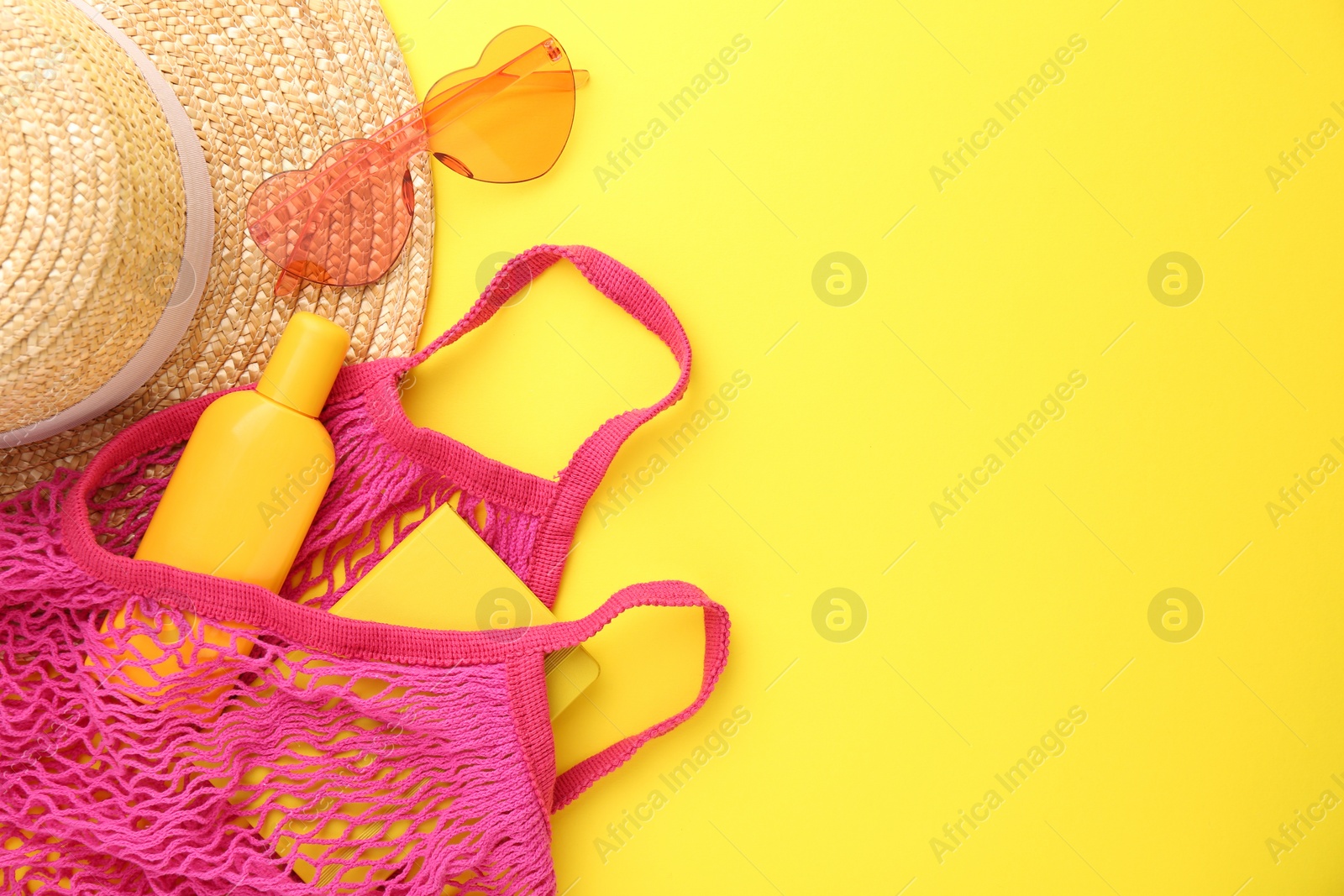 Photo of String bag with beach accessories on yellow background, flat lay. Space for text