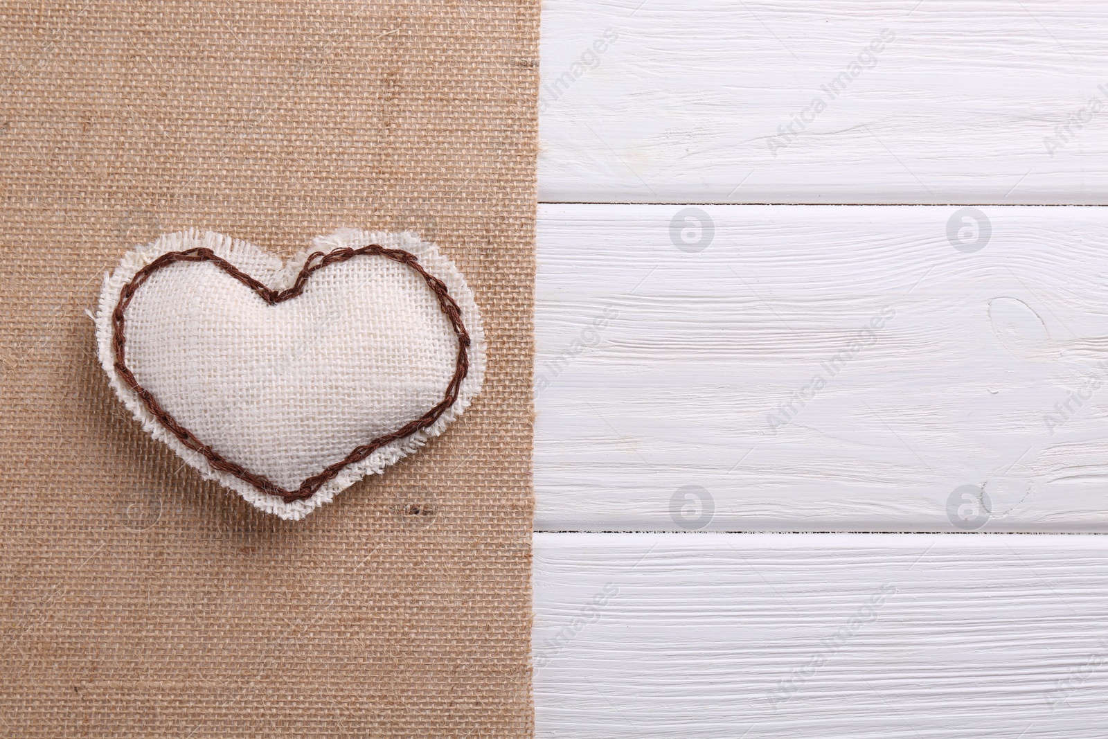 Photo of Heart made of burlap fabric with brown stitches and cloth on wooden table, top view. Space for text