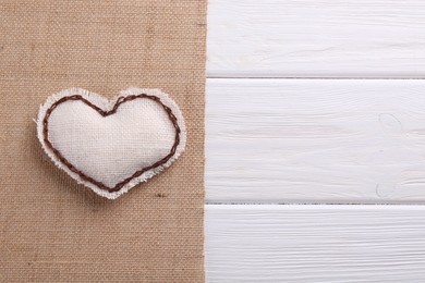 Heart made of burlap fabric with brown stitches and cloth on wooden table, top view. Space for text