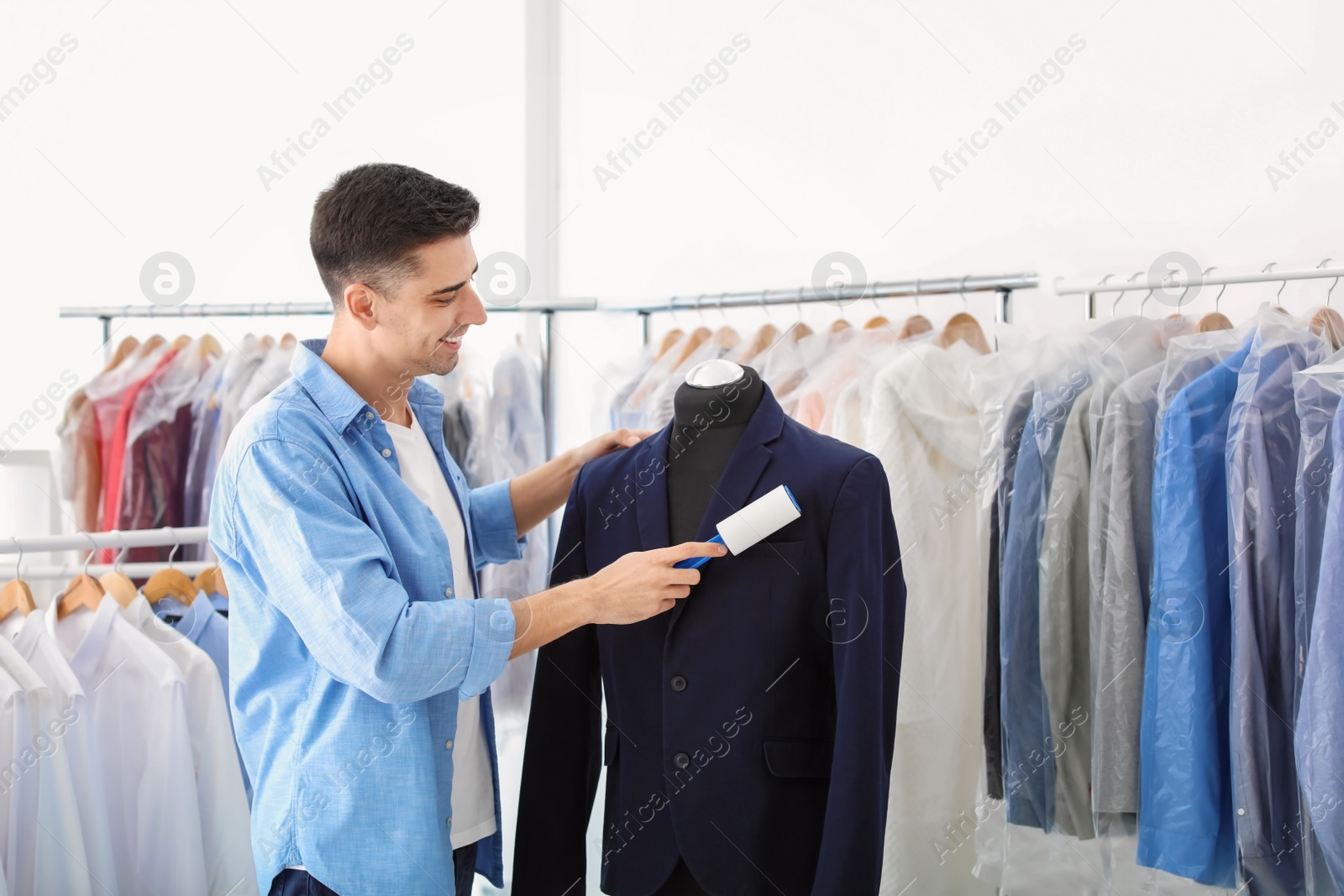 Photo of Young man removing dust from jacket with lint roller at dry-cleaner's