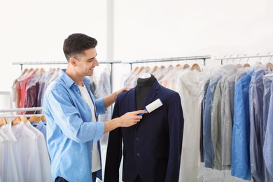 Photo of Young man removing dust from jacket with lint roller at dry-cleaner's