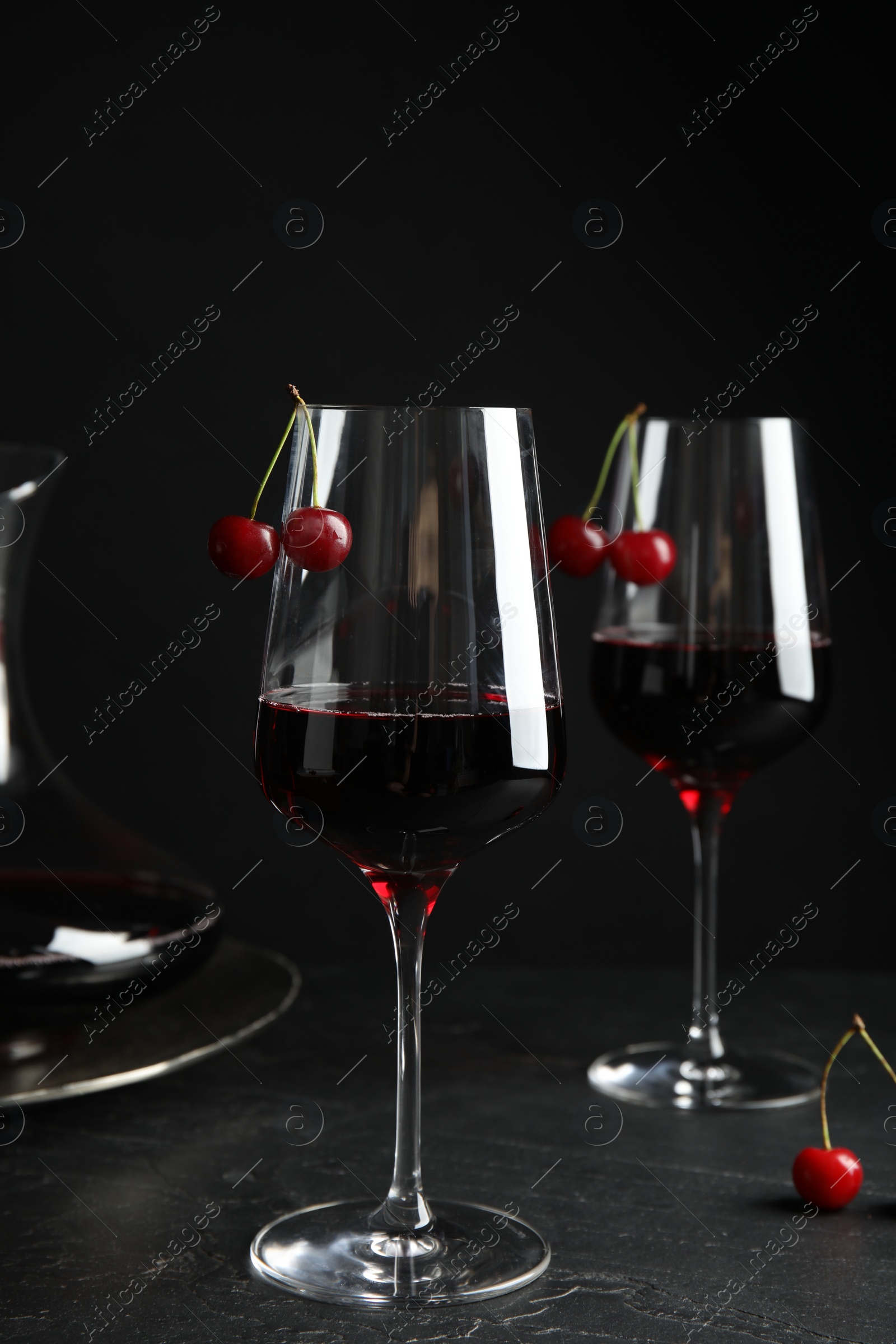 Photo of Delicious cherry wine with ripe juicy berries on grey table against black background