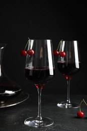 Delicious cherry wine with ripe juicy berries on grey table against black background