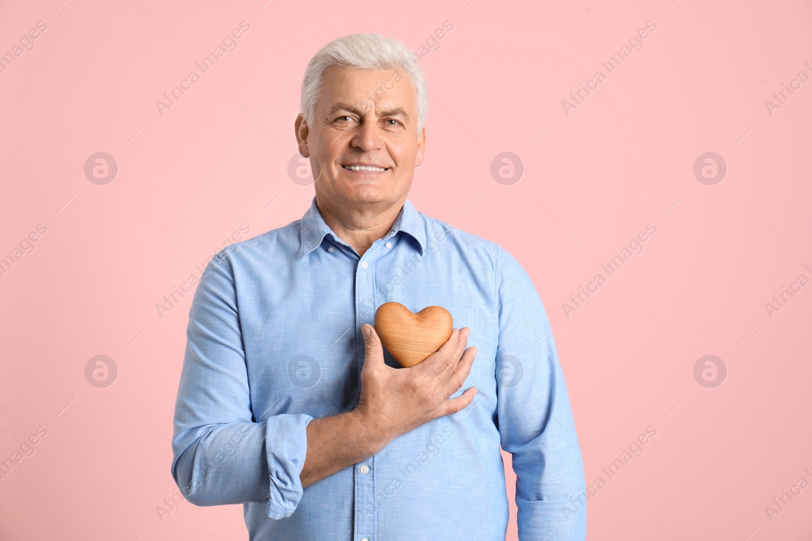 Photo of Happy mature man holding wooden heart on color background