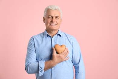 Photo of Happy mature man holding wooden heart on color background