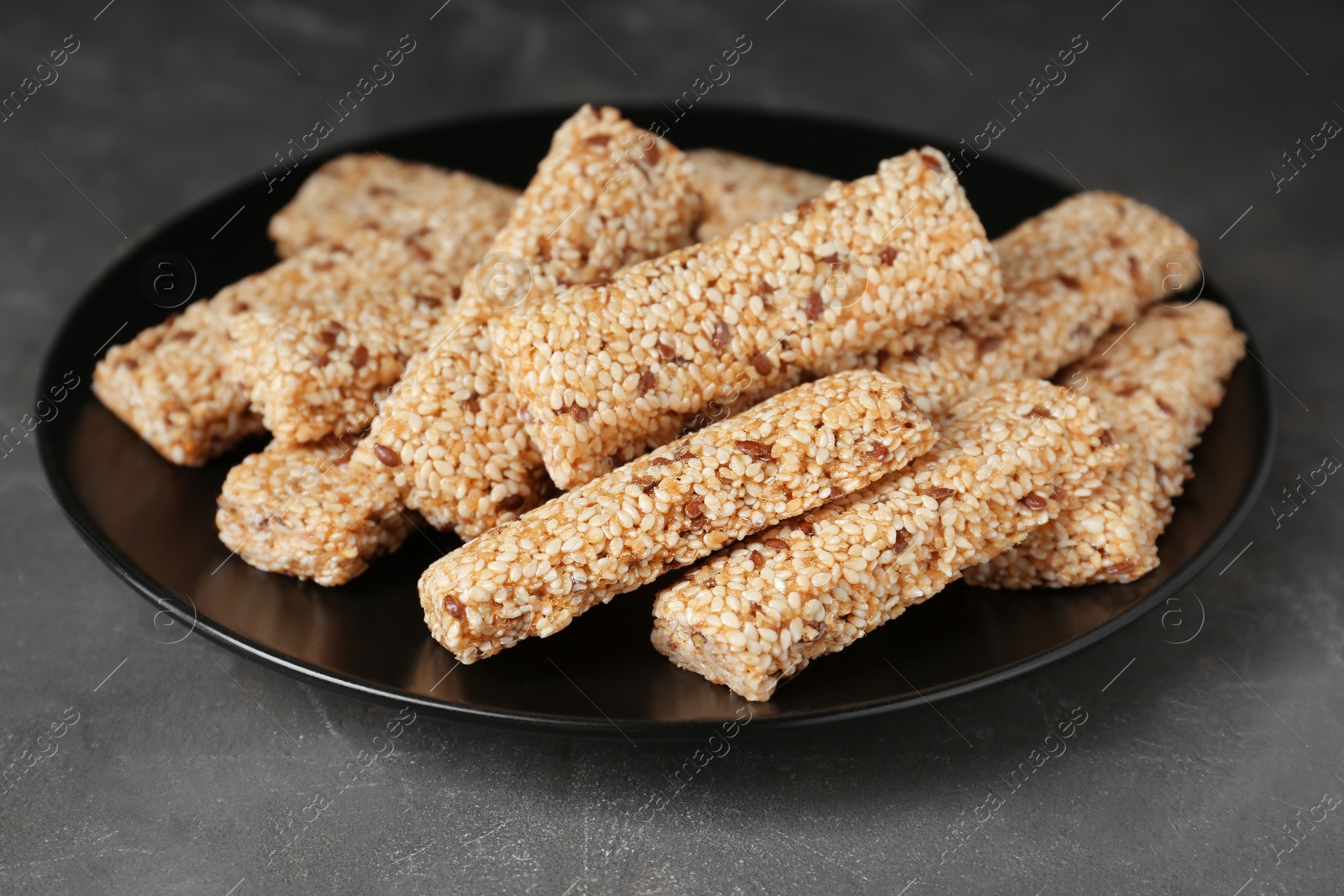 Photo of Plate with tasty sesame seed bars on dark grey table, closeup