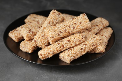 Photo of Plate with tasty sesame seed bars on dark grey table, closeup