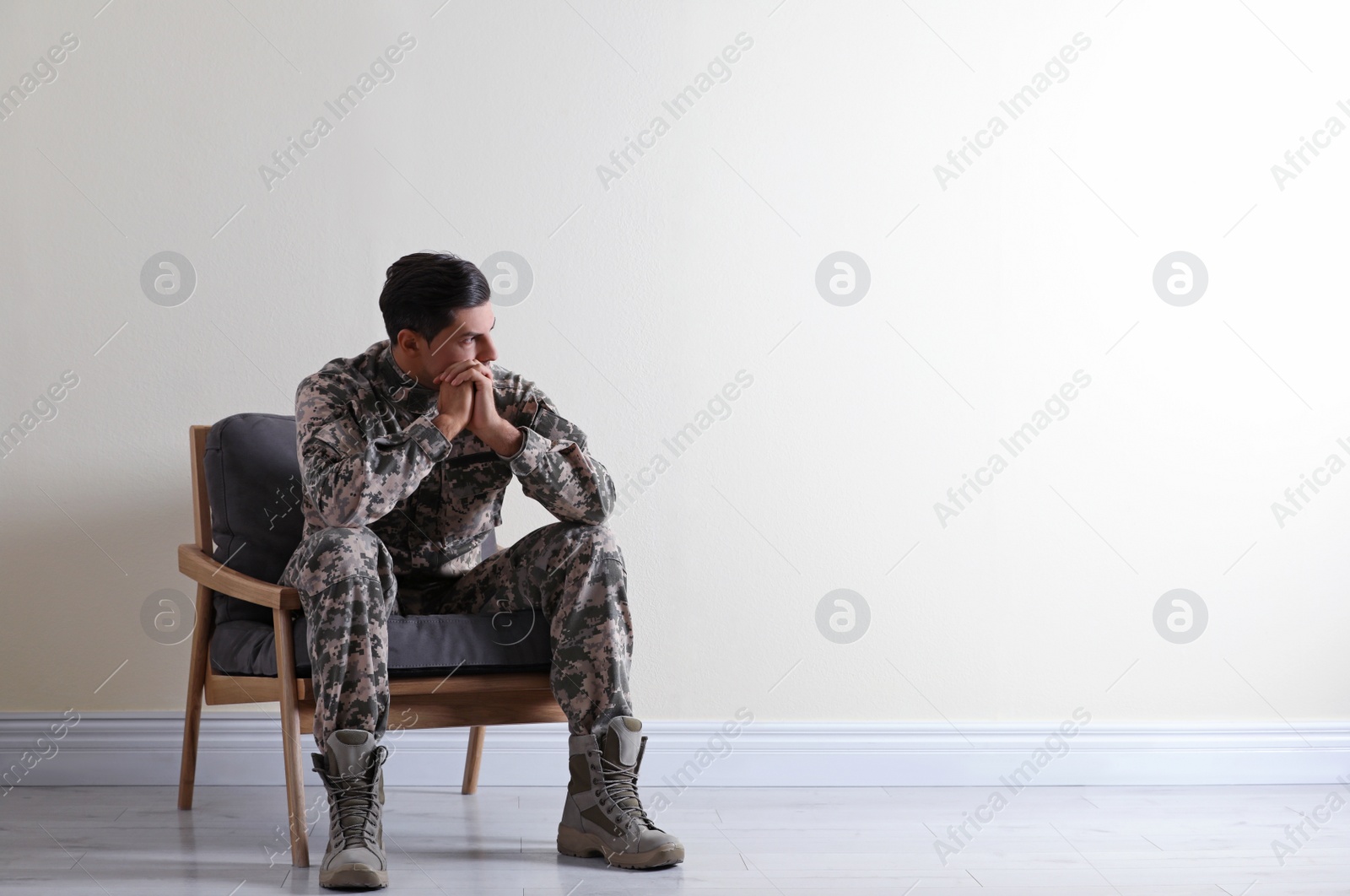 Photo of Stressed military officer sitting in armchair near white wall indoors. Space for text