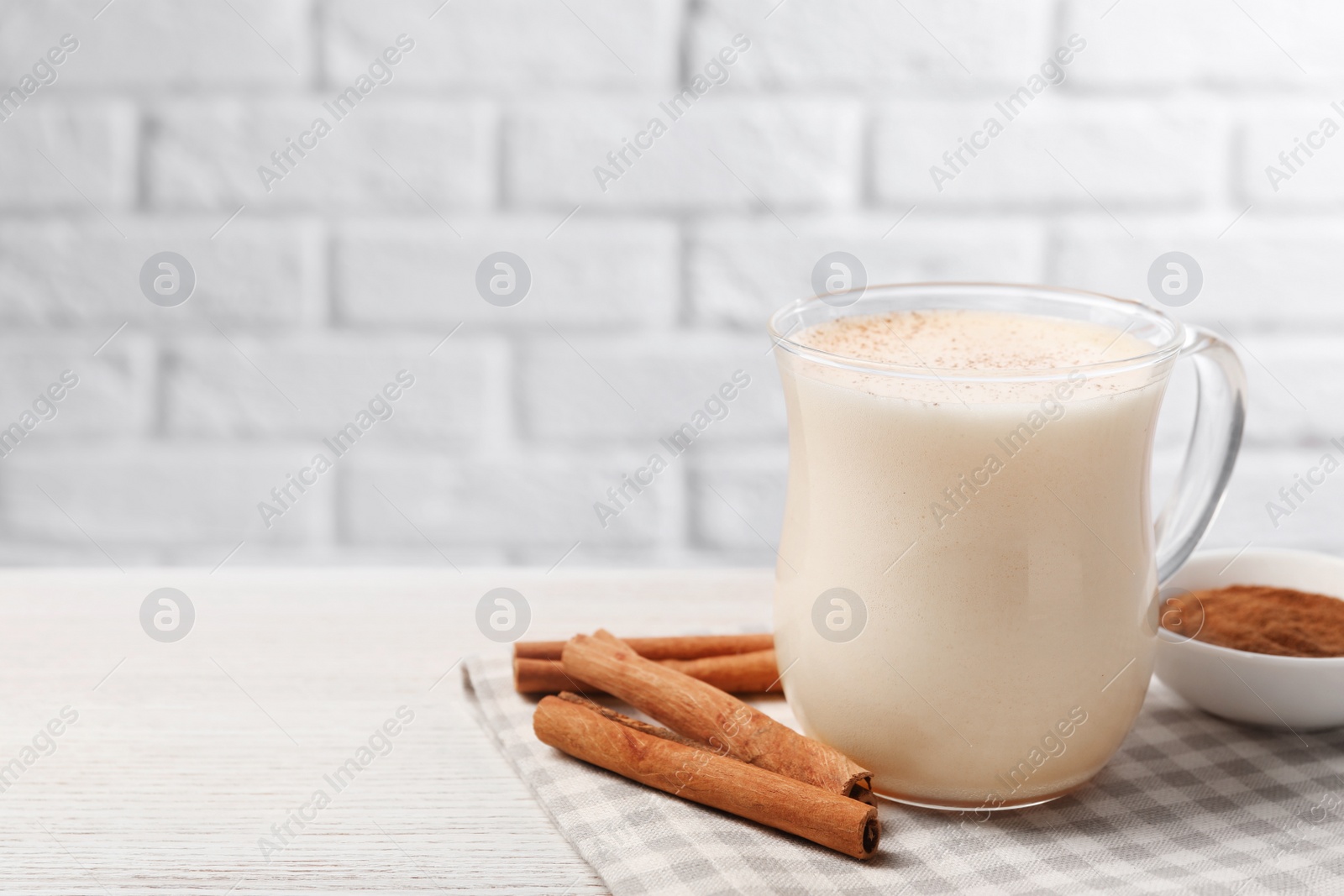 Photo of Delicious eggnog with cinnamon on wooden table, space for text