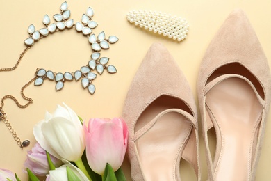 Photo of Stylish shoes, beautiful flowers and accessories on beige background, flat lay