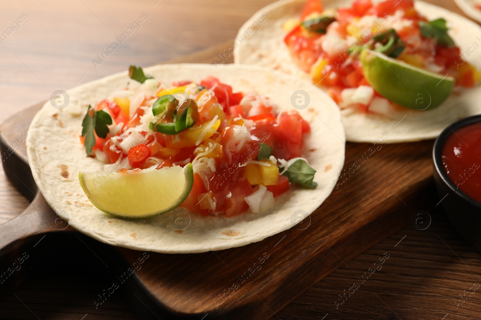 Photo of Delicious tacos with vegetables, lime and ketchup on wooden table, closeup