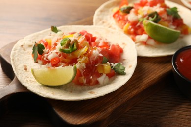 Photo of Delicious tacos with vegetables, lime and ketchup on wooden table, closeup