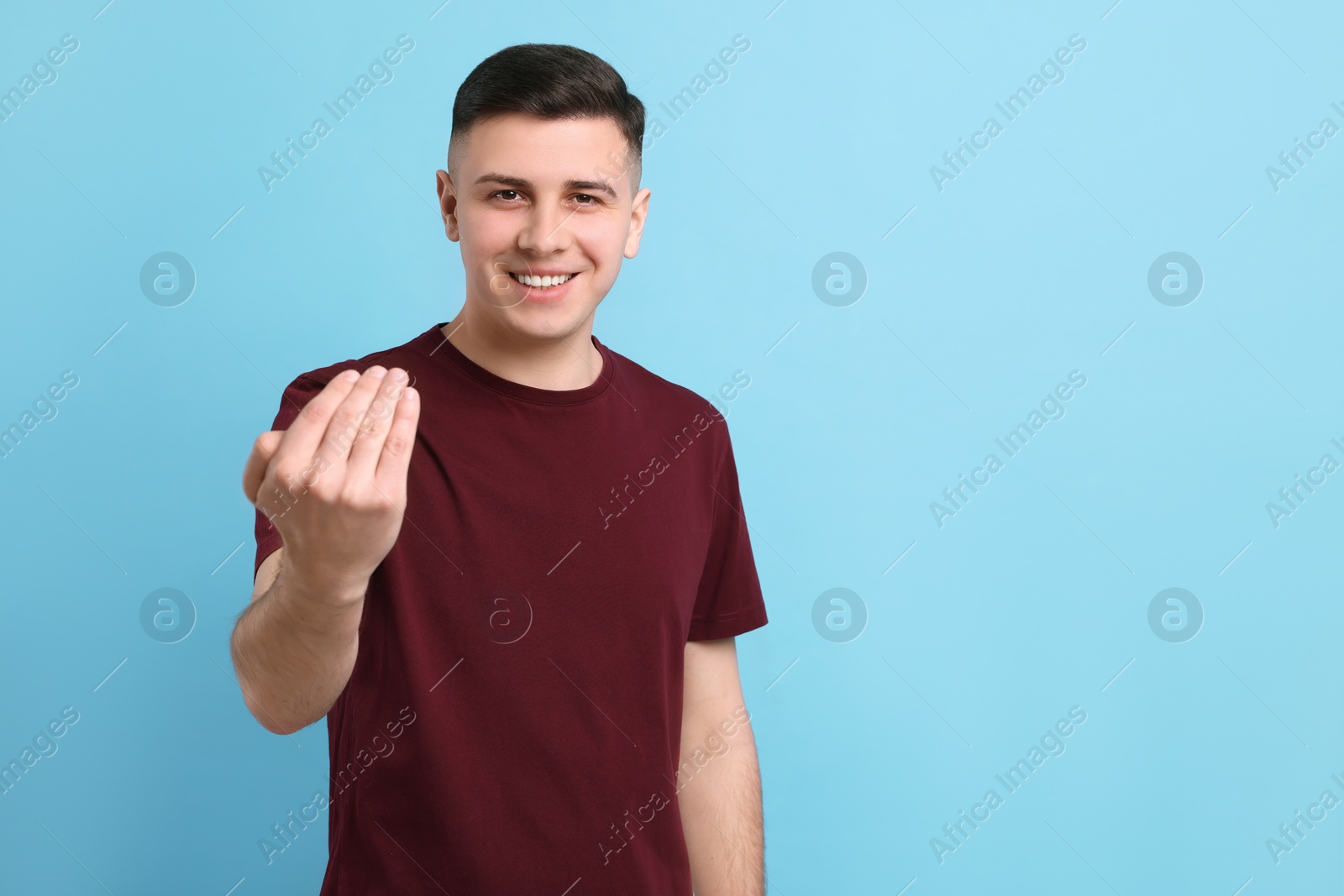 Photo of Handsome man inviting to come in against light blue background. Space for text