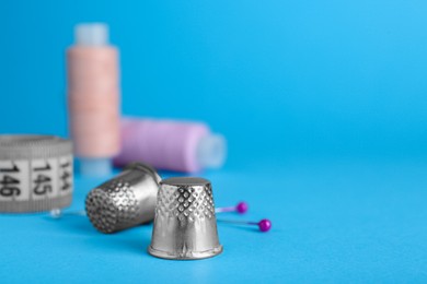 Photo of Silver thimbles on light blue background, space for text. Sewing accessories