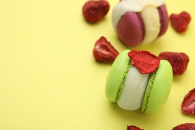 Photo of Delicious macarons and dry strawberries on yellow background, closeup. Space for text