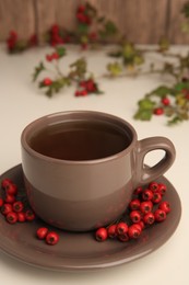 Aromatic hawthorn tea in cup and berries on beige table, closeup