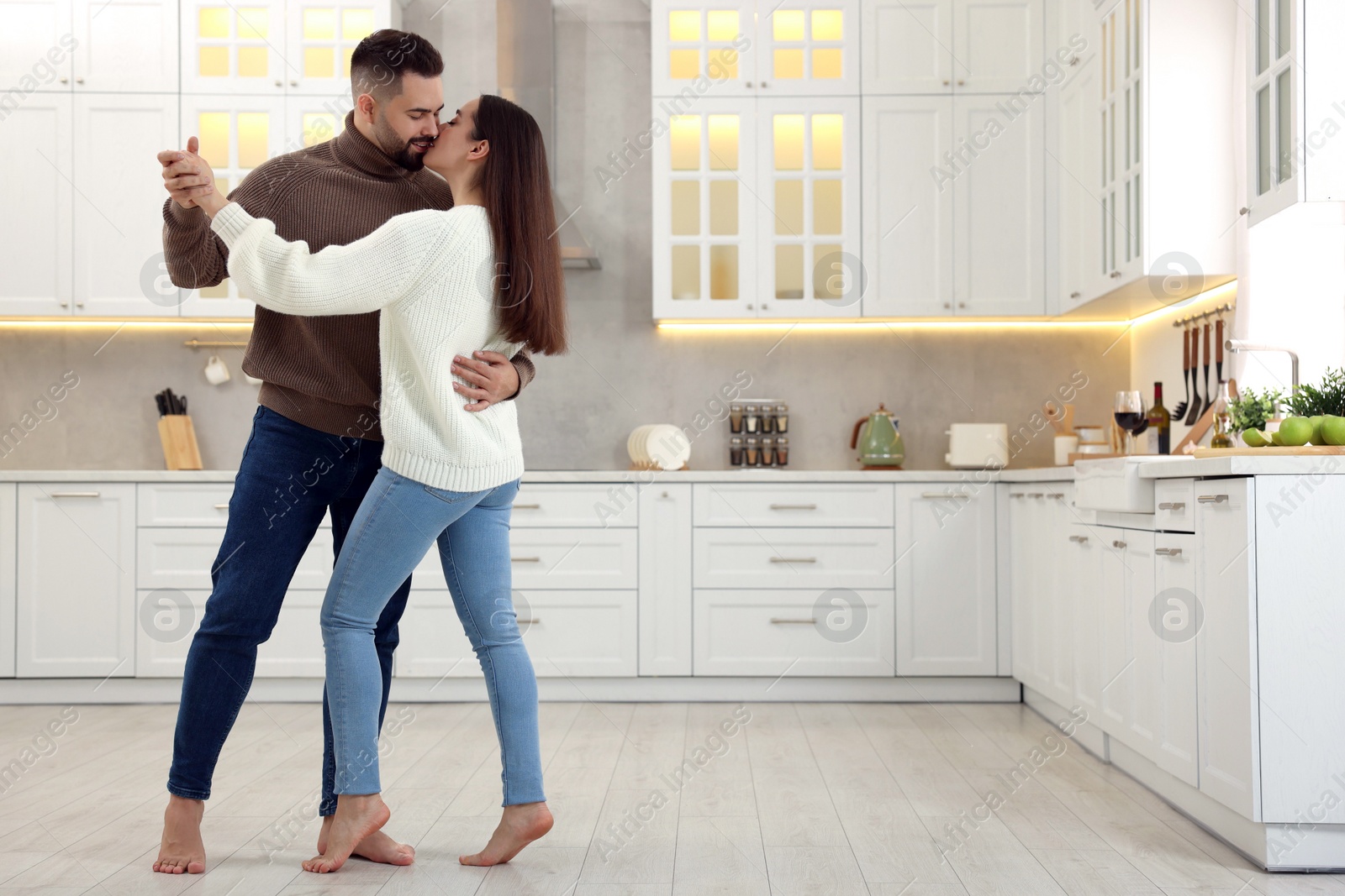 Photo of Affectionate young couple dancing and kissing in kitchen. Space for text