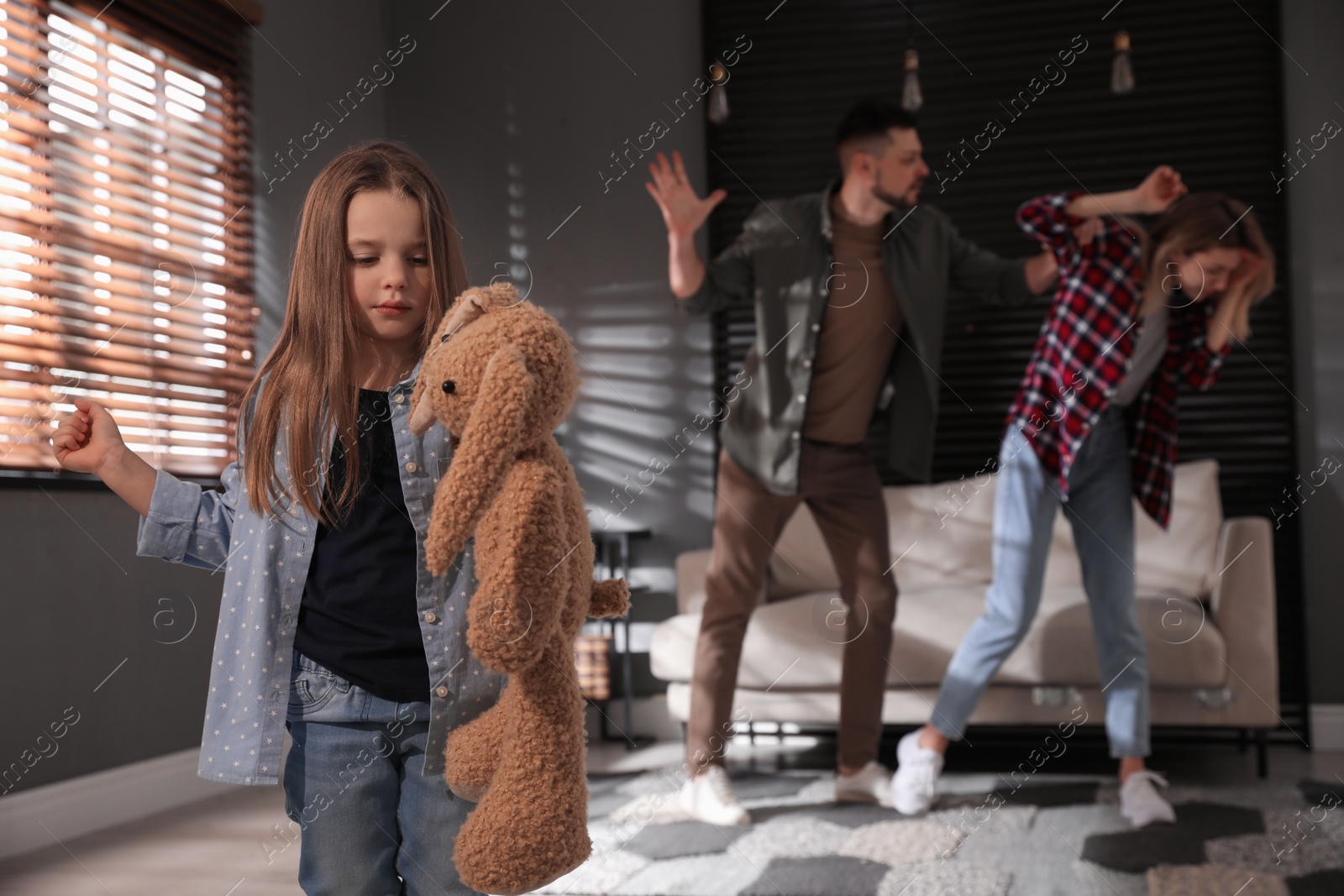 Photo of Little girl punishing toy bunny while her parents fighting on background, space for text. Domestic violence