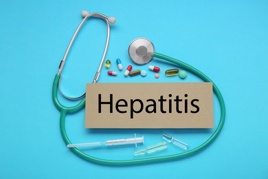 Cardboard with word Hepatitis and medical supplies on light blue background, flat lay