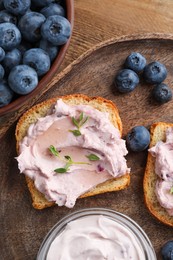 Photo of Tasty sandwiches with cream cheese, thyme and blueberries on wooden tray, flat lay