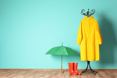 Umbrella, rain coat and boots near color wall with space for design