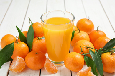 Photo of Glass of fresh tangerine juice and fruits on white wooden table