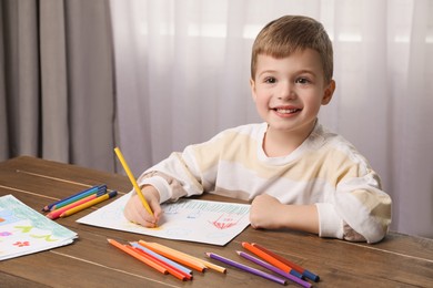 Photo of Cute little boy drawing with pencil at wooden table in room. Child`s art