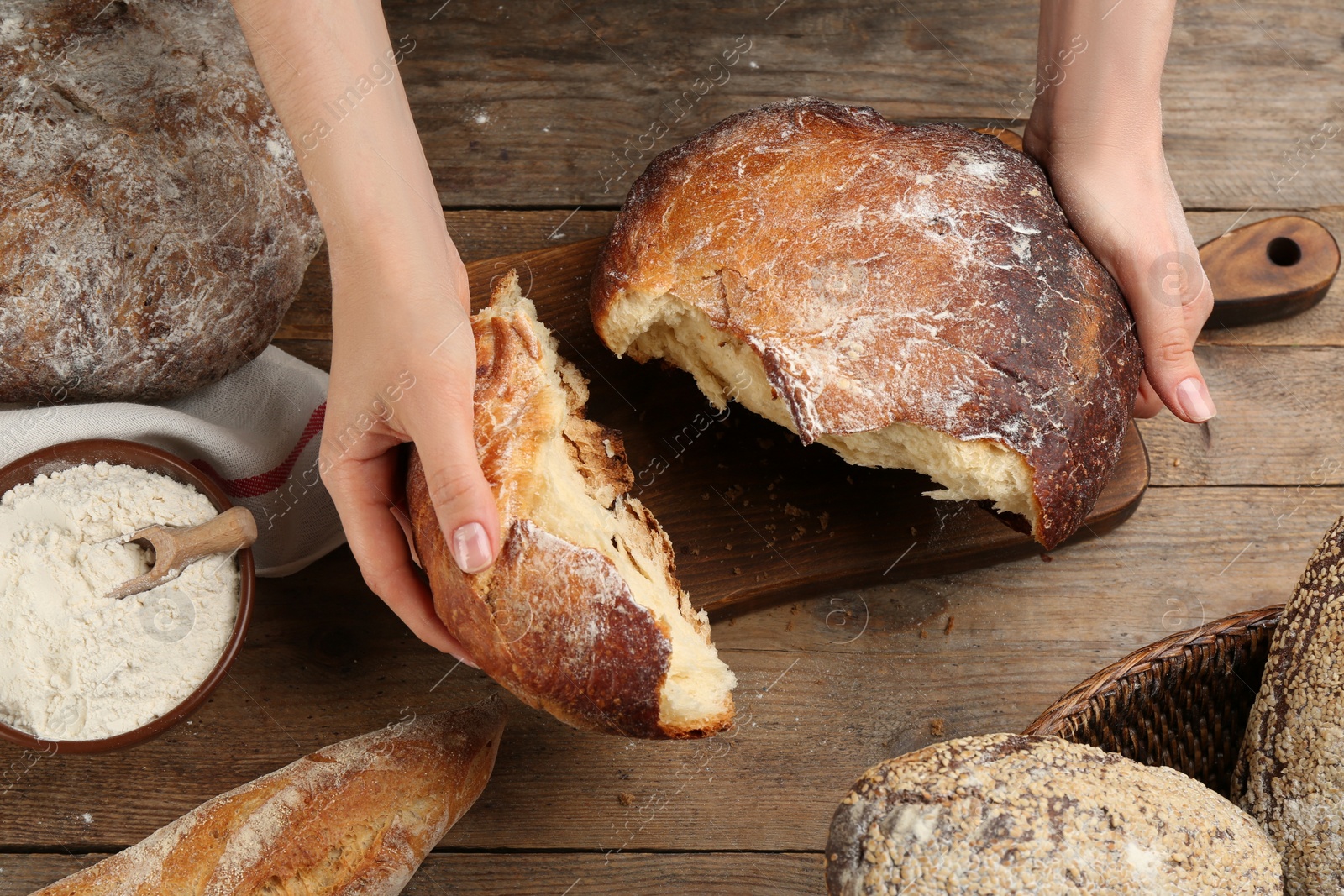 Photo of Woman breaking freshly baked bread at wooden table, closeup