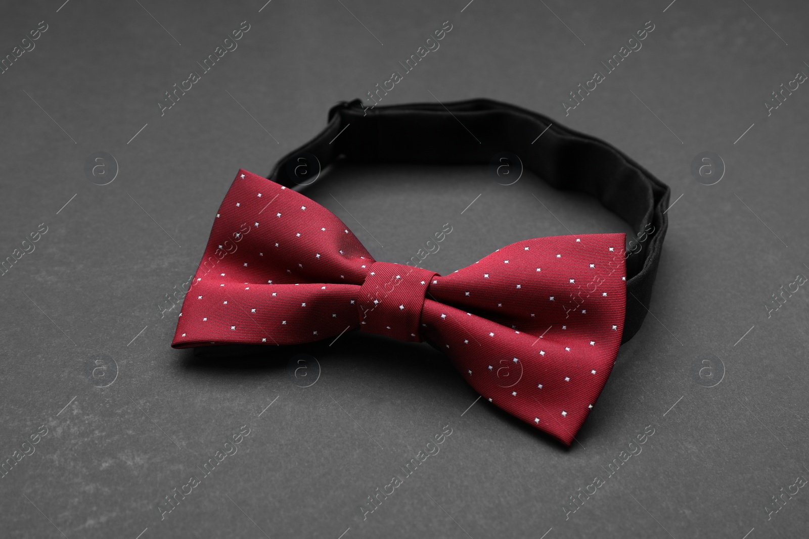 Photo of Stylish burgundy bow tie with polka dot pattern on black background