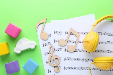 Wooden notes, music sheets, headphones and toys on light green background, flat lay. Baby song concept