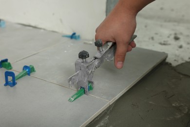 Photo of Man installing colorful wedges with plier on tiles, closeup