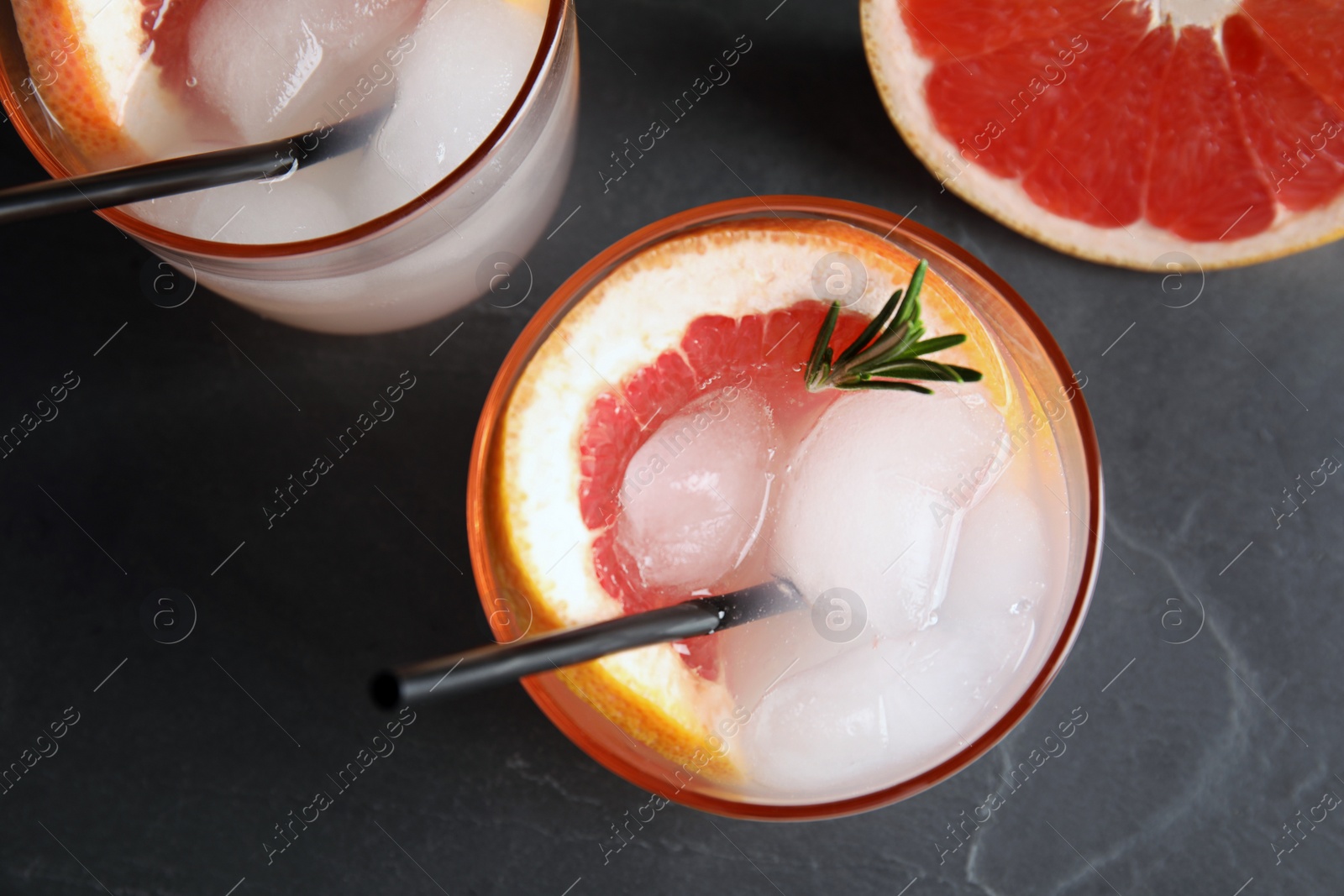 Photo of Glasses of cocktail and grapefruit slice on dark table, flat lay