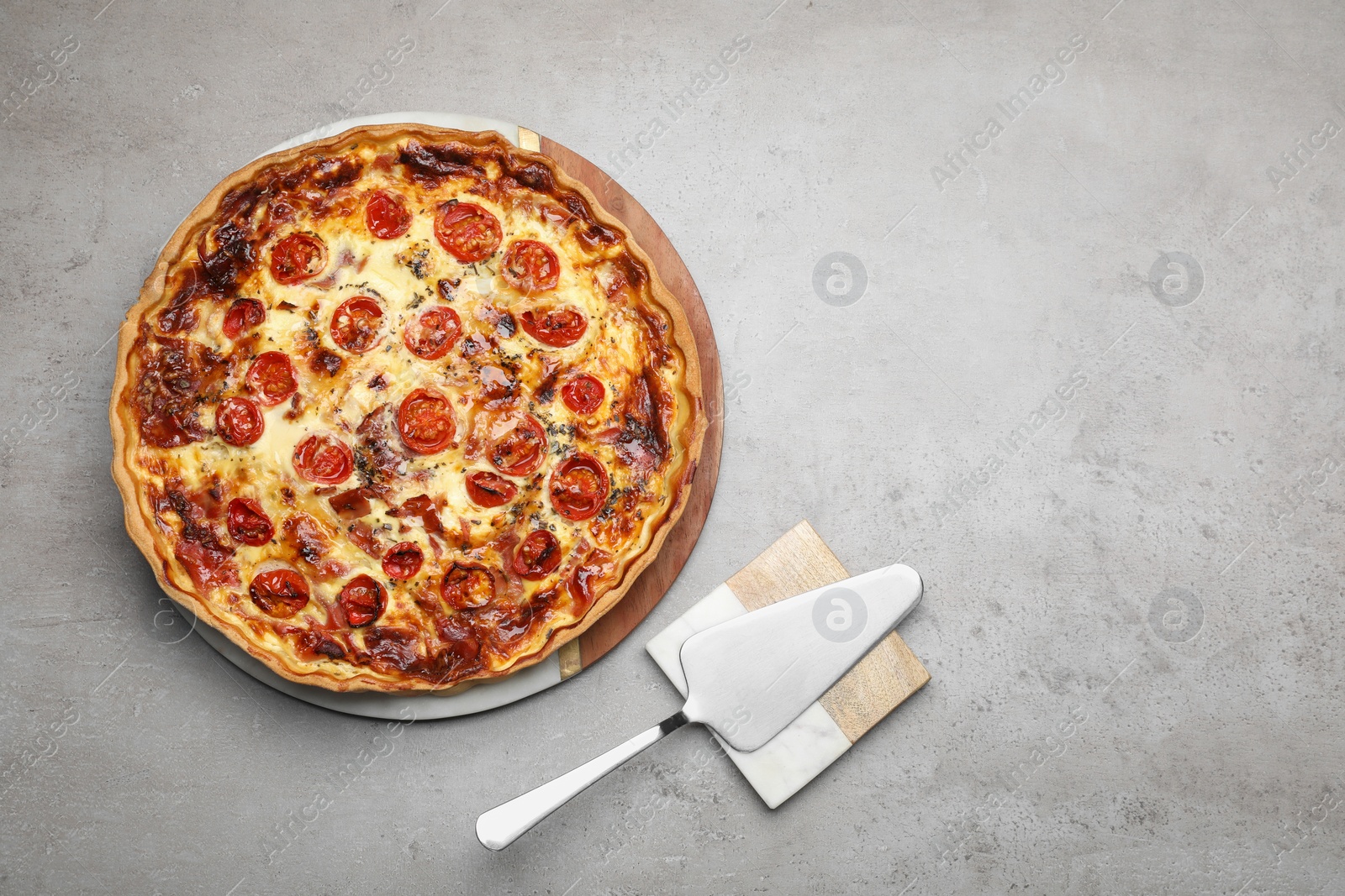 Photo of Delicious homemade prosciutto quiche and spatula on light gray table, flat lay. Space for text