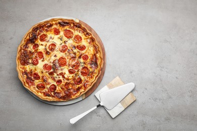 Delicious homemade prosciutto quiche and spatula on light gray table, flat lay. Space for text