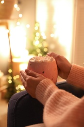 Photo of Woman holding cup of hot drink with marshmallows indoors, closeup. Magic Christmas atmosphere