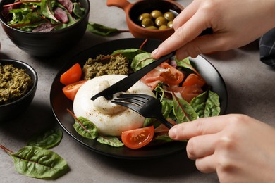 Photo of Woman eating delicious burrata salad at grey table, closeup